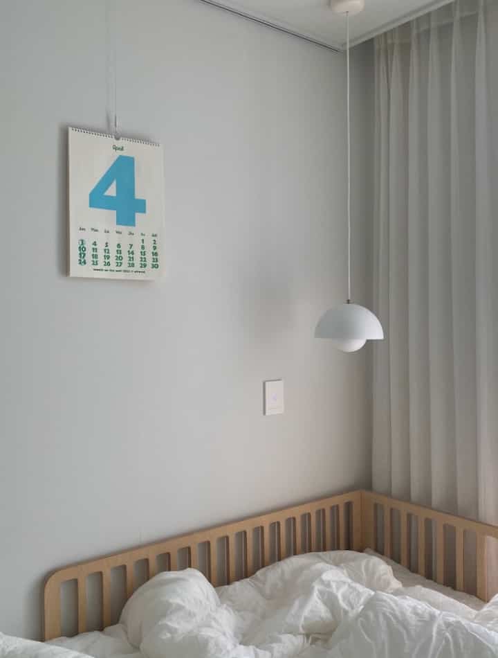 Bright white and wood tone kids' room featuring a natural modern crib and chiffon curtains