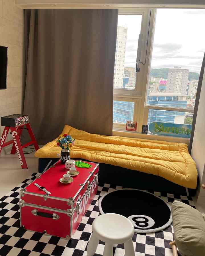 黒、赤、黄色が調和した狭いリビングルーム、チェッカーボードの床とスツール、黄色いマットレスが配置された印象的な空間