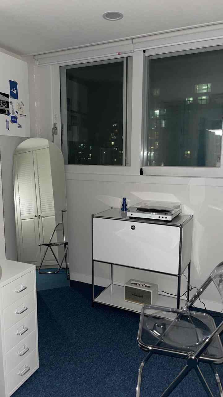 白い壁と青いカーペットのミッドセンチュリーモダンなワークスペース、チェストとアーチ型の全身鏡、透明な椅子が配置された印象的な空間