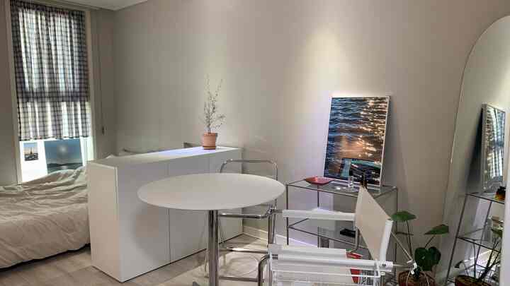 白を基調とした二人暮らしのための空間分けされた部屋、丸テーブルと透明椅子、額縁、植物が配されたシンプルモダンなインテリア