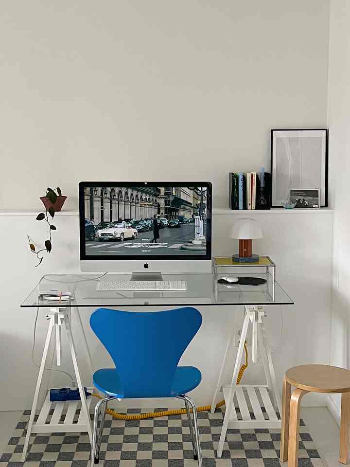 White-toned home office featuring a blue chair and glass desk with minimalist decor for focused work