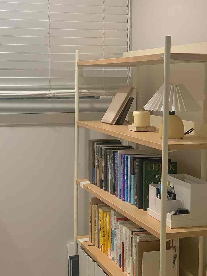 Natural wood tone and white blinds combine in a neat home office bookshelf and shelving space