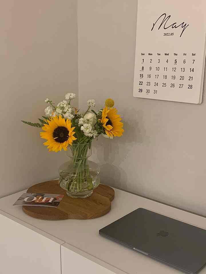 Simple home office with a white wall and desk featuring a wood tone tray and a sunflower vase
