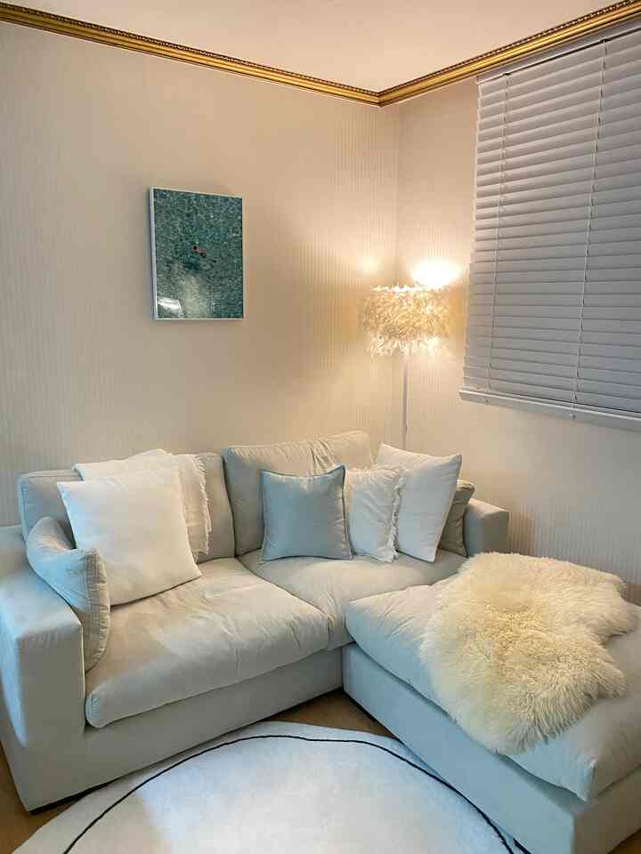 Soft white-toned living room featuring a wide sectional sofa at center and cozy ambient lighting creating a warm atmosphere