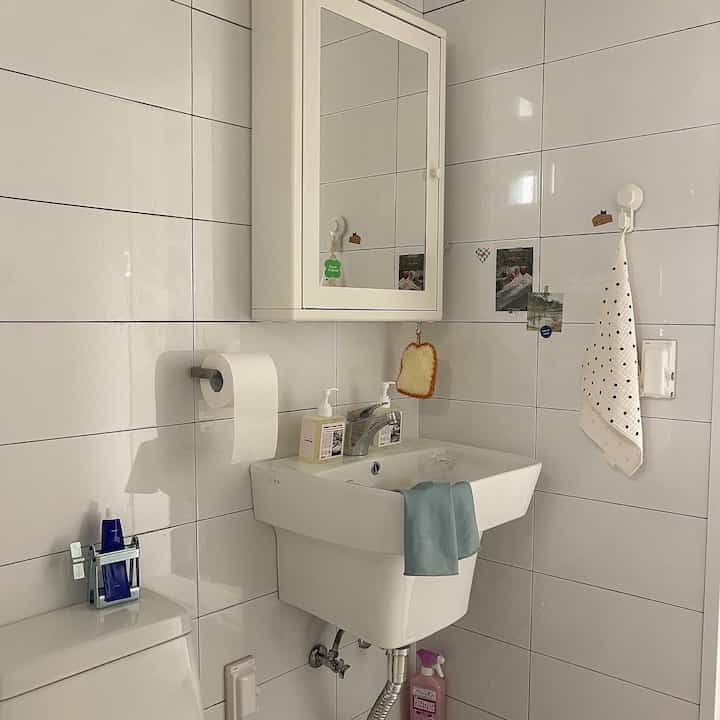 白いタイル壁と洗面台、壁掛けキャビネットが配置されたコンパクトなバスルームの雰囲気のあるインテリア