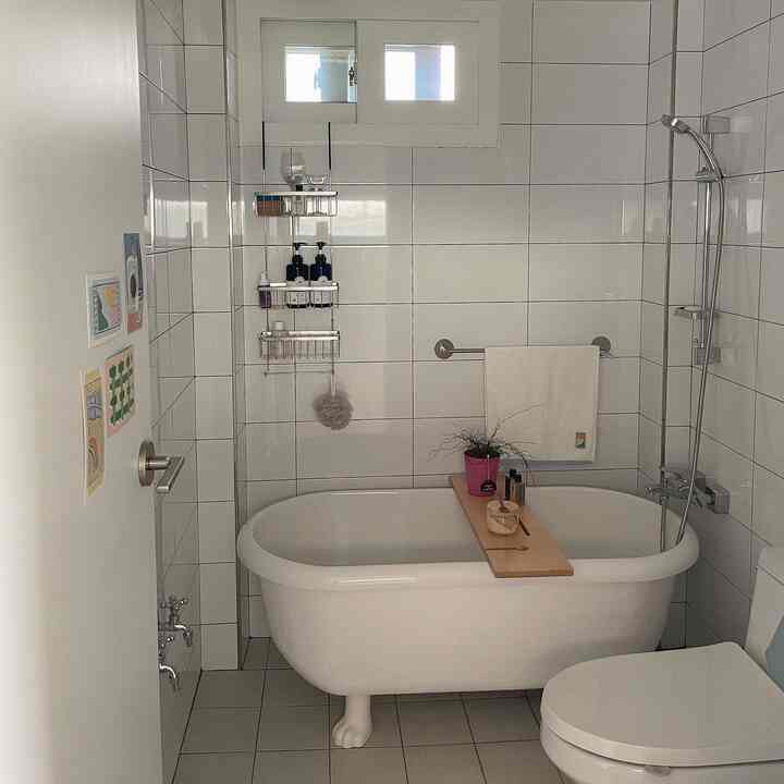 A white-tiled bathroom featuring a cat-paw bathtub with a wooden tray, creating a simple and clean atmosphere