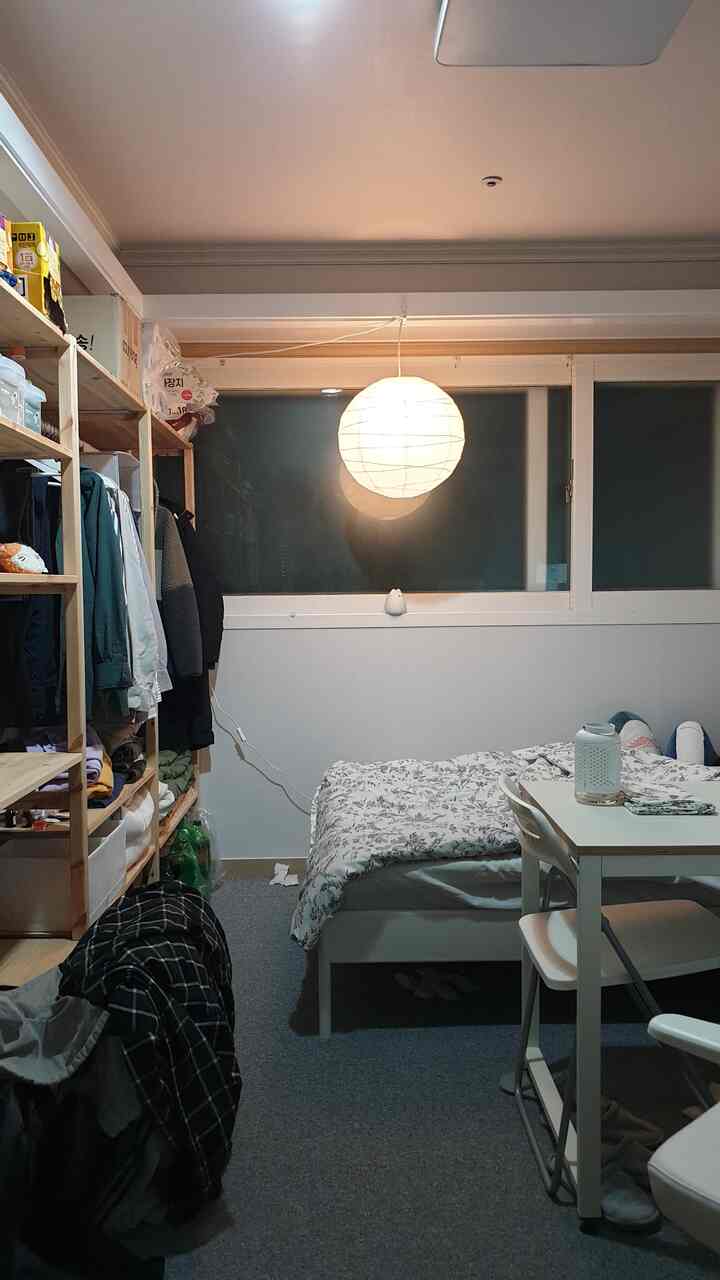 White and gray toned studio bedroom featuring bed, table, and shelving in a compact and practical space
