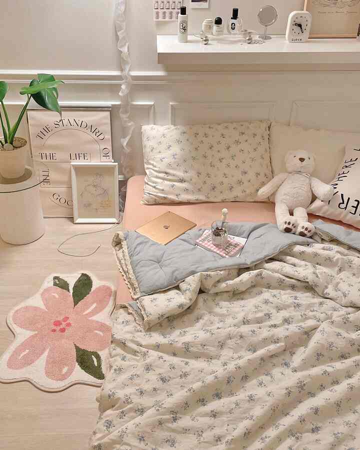 白とピンクのトーンの寝室、花柄の寝具と枕、テディベア、植物が配置された印象的な空間