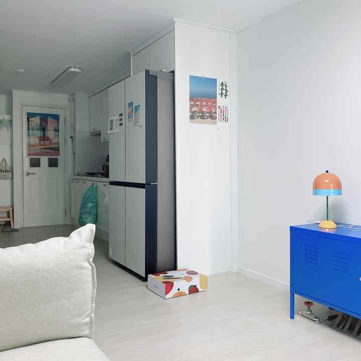 ホワイトの壁と床、鮮やかなブルーのキャビネットとカラフルなランプが配置されたミッドセンチュリーモダン風のリビングルーム