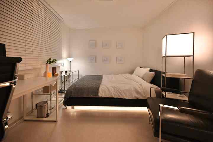 Modern single bedroom in white and black tones featuring bed, desk, and armchair in a simple setting