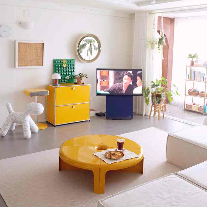 A white and yellow toned living room featuring mid-century modern furniture and plants creating a cozy atmosphere