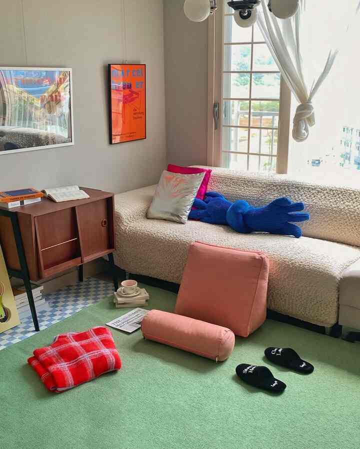 Beige-toned walls and sofa with green rug, vintage furniture, and cushions arranged in a cozy living room space