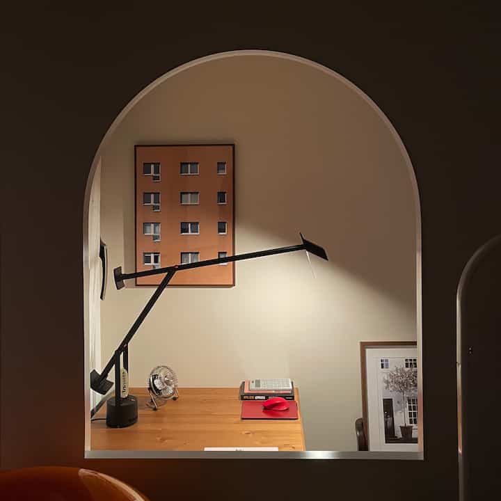 Natural-toned wood desk in a compact walk-in closet and study space featuring an arched room divider window, cozy indoor atmosphere