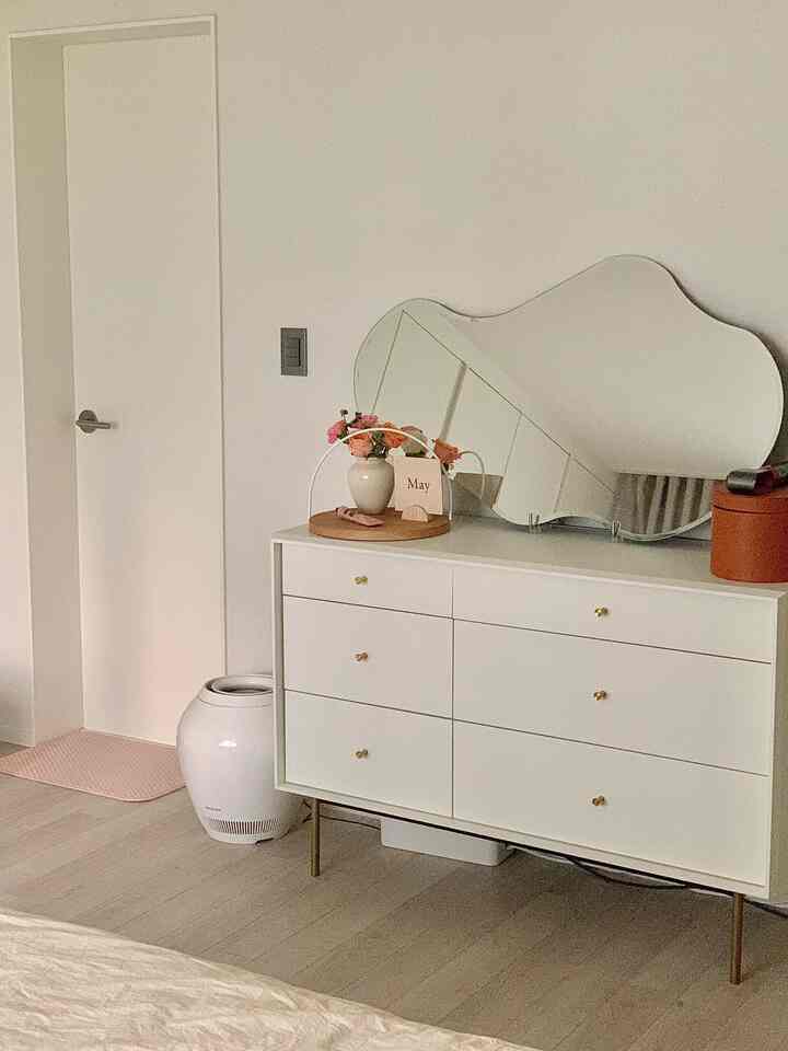 White-toned bedroom featuring a wide dresser with mirror and natural sunlight creating a cozy atmosphere
