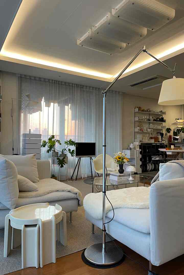Natural-toned living room with white sofas centrally placed, a floor lamp, and large curtained window creating cozy atmosphere
