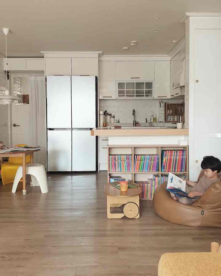 White and natural tone kitchen and living room featuring bookshelf and bean bag, creating a cozy family space