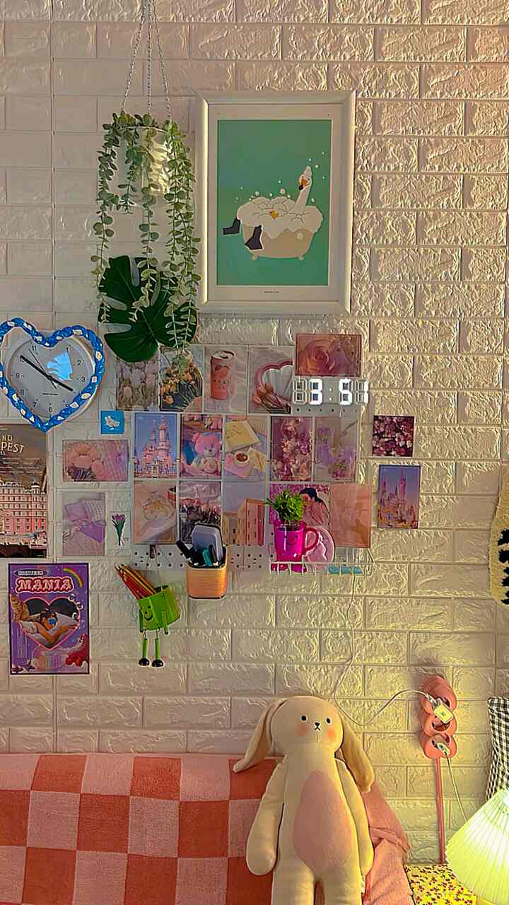 ピンクとアイボリーの色調の子供部屋の壁に額縁やLED時計、フロアランプ、植物、チェックのブランケットが配置された雰囲気のあるインテリア