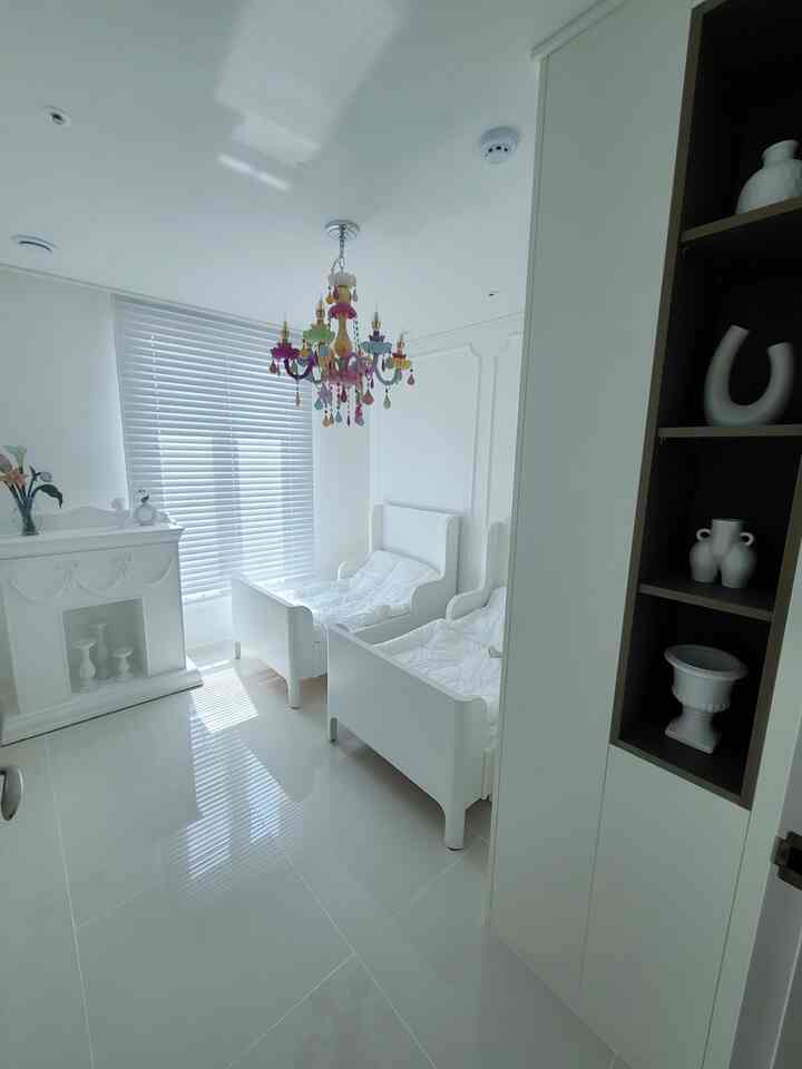 Bright white kids' room featuring two children's beds and a colorful chandelier creating a cheerful atmosphere
