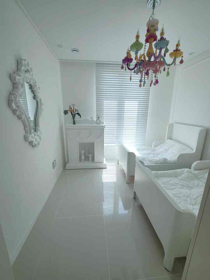 明るいホワイトトーンの子供部屋、二つの子供用ベッドとカラフルなシャンデリアが配置されたシンプルな空間