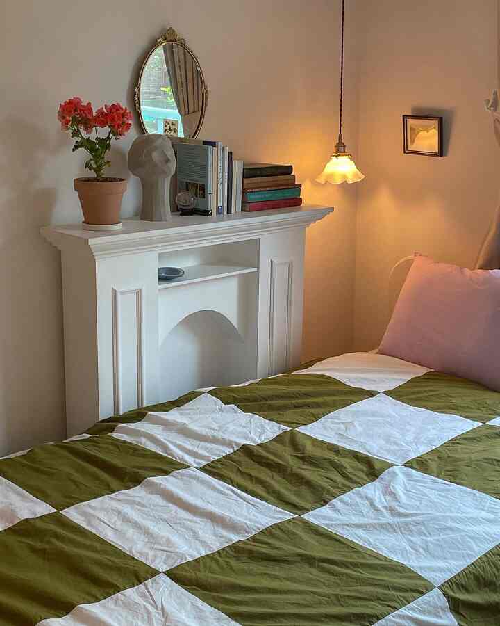 Cozy bedroom with white walls and fireplace, featuring a green and white checkered duvet cover and vintage pendant lighting