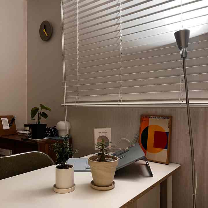 Mid-century modern home office with white and wood tones, featuring plants and a poster for a simple and cozy workspace