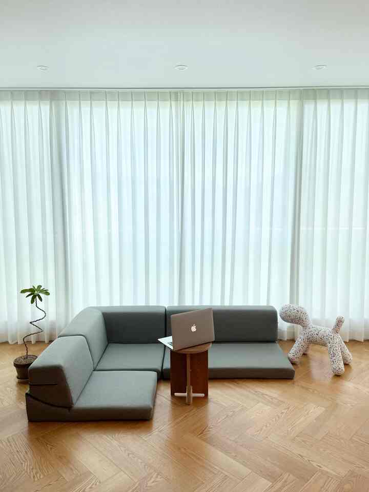 Compact natural modern living room with light wood flooring, white curtains, gray sofa, and round side table
