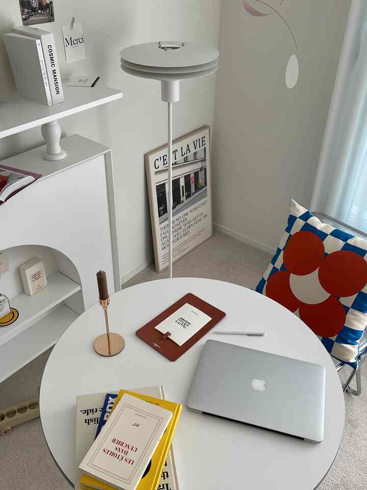 Modern studio apartment home office in white and gold tones featuring round table, laptop, books and colorful patterned cushion