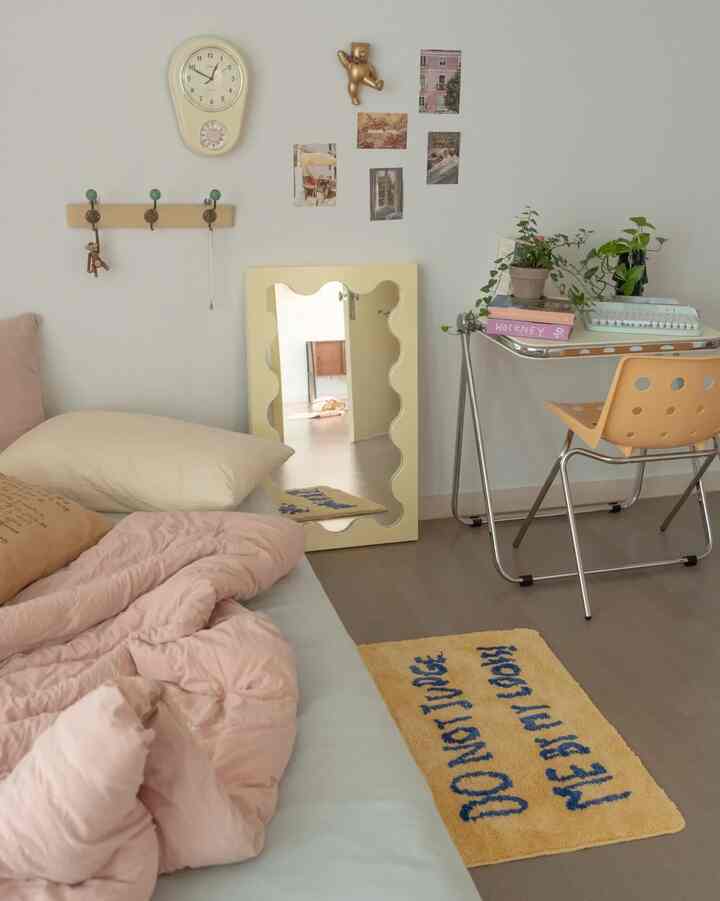 Beige and pink toned bedroom featuring bed, desk, wavy mirror, and plants, creating a cozy natural atmosphere