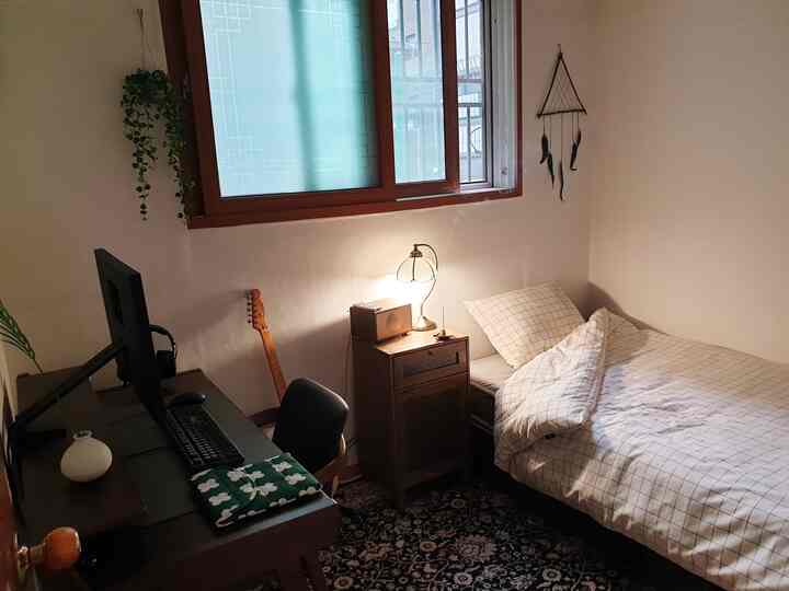 White walls and brown wood-tone furniture in a single household bedroom, featuring a computer desk and bed in a cozy space