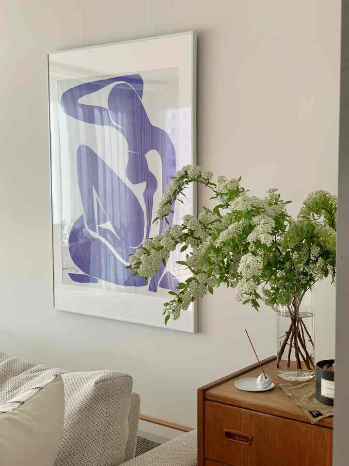 Natural-toned living room featuring beige sofa, wooden sideboard with transparent vase of white flowers, and blue silhouette framed art creating cozy atmosphere