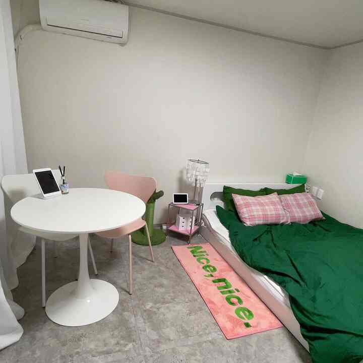 ホワイトとグリーンのトーンの6畳寝室、円形ダイニングテーブルとピンクのチェック柄枕があるベッドを配したシンプルモダンな空間