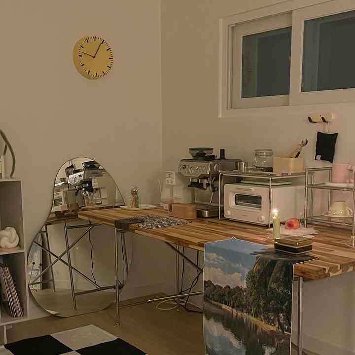 ナチュラルな木目調とホワイトの作業スペース、コーヒーマシン、壁時計、ユニークな鏡が配置された雰囲気のあるおうちカフェ空間
