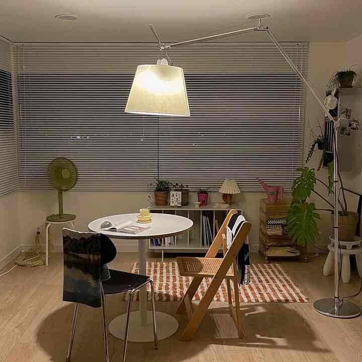 温かみのあるブラウンとホワイトのトーンのダイニングルーム、円形テーブルとアルノチェア、ラグ、フロアランプが配置された印象的な空間