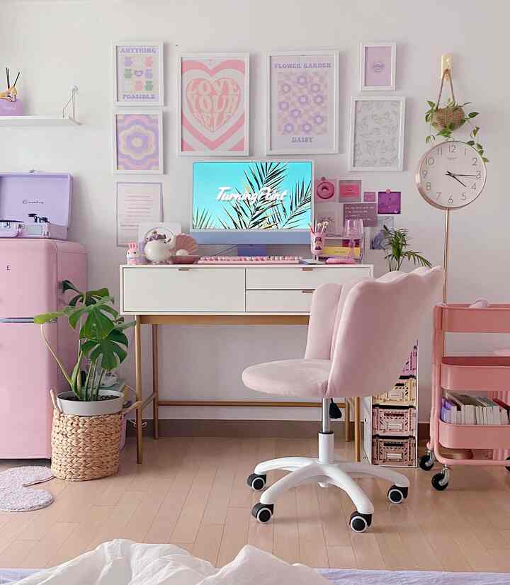 Pastel pink and white home office featuring a desk with velvet chair, colorful wall art, and plants creating a cozy workspace