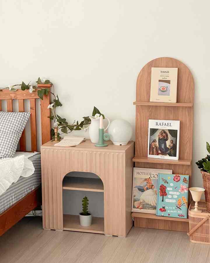 Light wood tone bedroom with white walls, featuring a checkered bed and wooden mini fireplace cabinet and shelf conveying a calm atmosphere