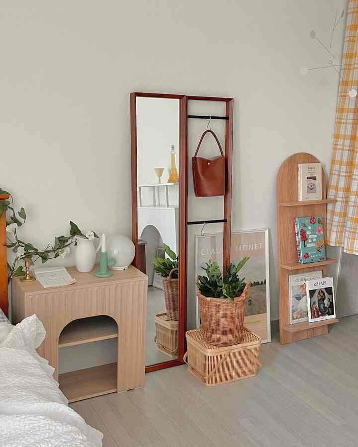 ナチュラルな木目調とホワイトの寝室、全身鏡とラタンの鉢植え、書棚が配置された雰囲気のあるインテリア