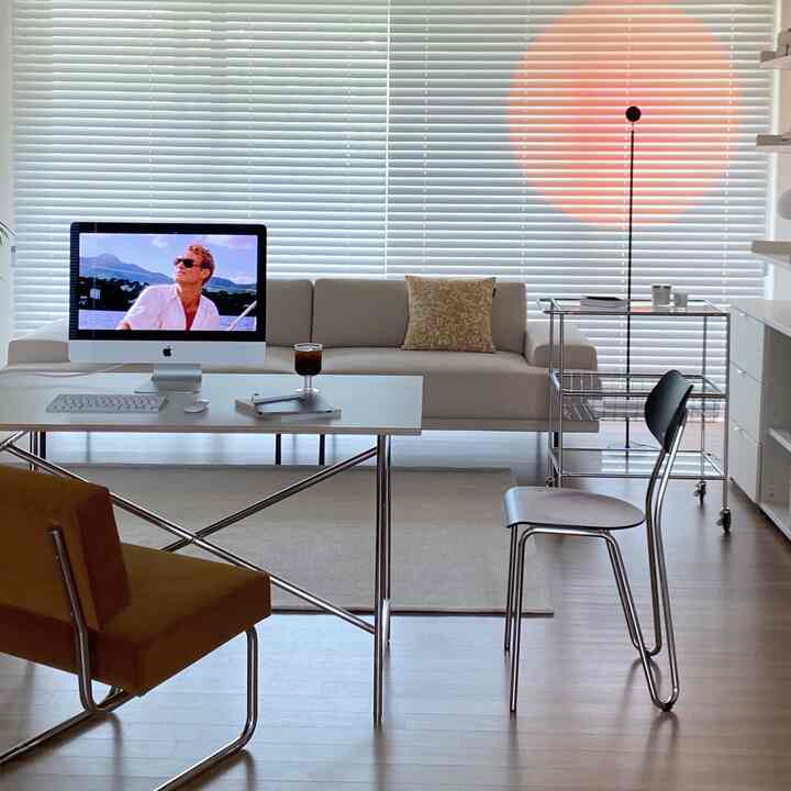 A white and modern toned living room home office featuring an iMac desk, beige rug, and steel furniture in a clean layout