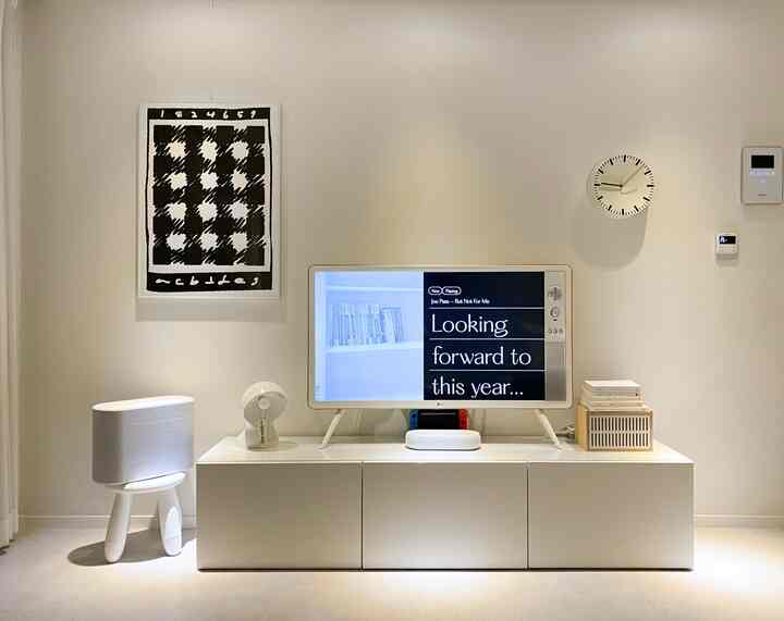 モノトーンの白と黒が調和したリビング、テレビ台、額縁ポスター、子供用スツールとテーブルランプが配置されたミニマルなインテリア