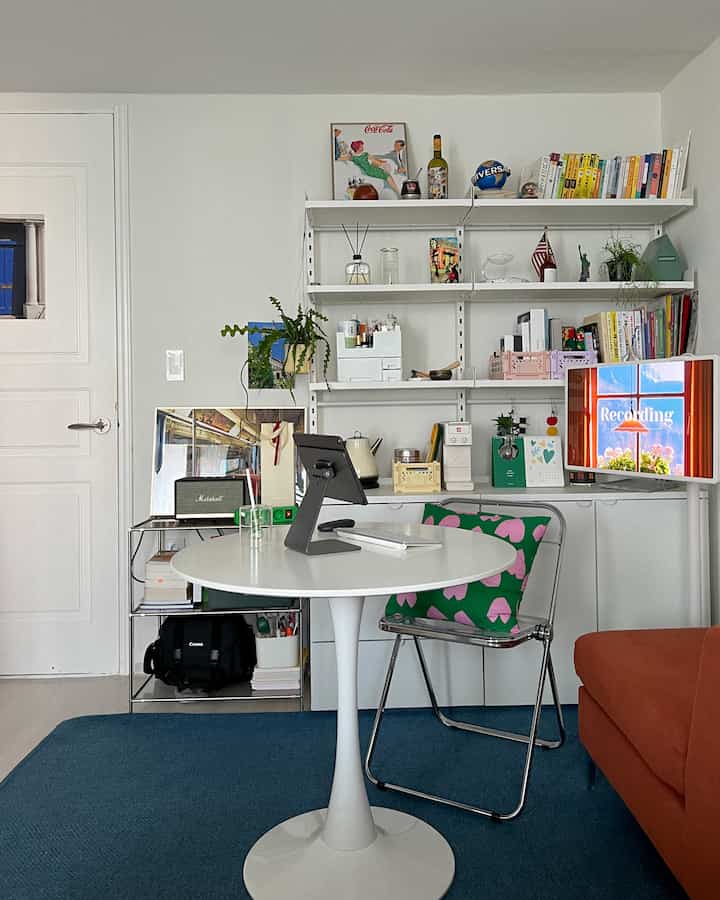 Sky blue rug and white walls define this studio home office featuring a round table with an iPad stand, creating a neat and modern study space