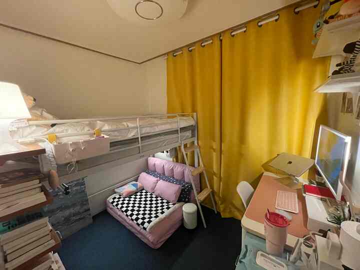 Small room with white walls and yellow curtains featuring a loft bed above a pink sofa and desk, creating a cozy atmosphere