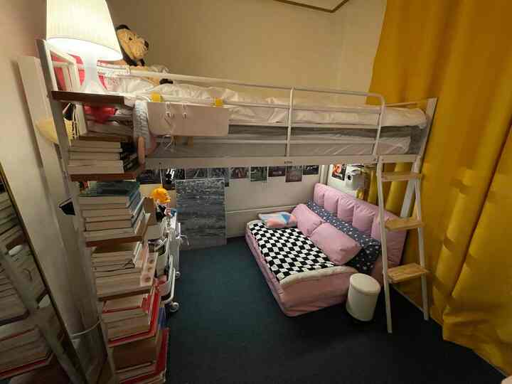 黄色い遮光カーテンとピンクのソファベッドが配置された、小さな部屋で、ロフトベッドと本棚がある雰囲気のあるインテリア