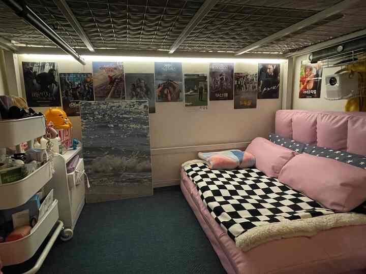 Small home cinema room with pink sofa bed and movie posters, featuring LED line lighting creating cozy atmosphere