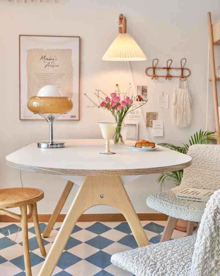 暖かい木目調とホワイトのダイニングルーム、ミッドセンチュリーモダン風のダイニングテーブルと椅子、壁面照明やポスターが調和した居心地の良いおうちカフェ空間