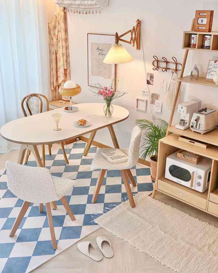 A white and blue checkered rug anchors a dining room featuring natural wooden furniture and wall sconce lighting, blending dining and home cafe elements