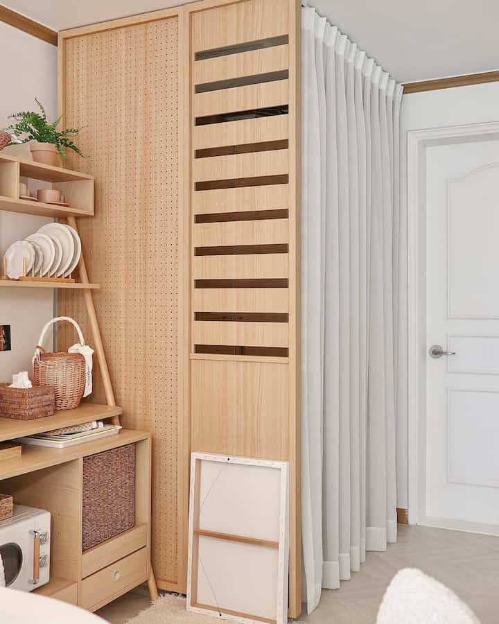 Natural wood tone entrance area with a white pleated curtain and wooden room divider, showcasing a clean and cozy self-interior style.