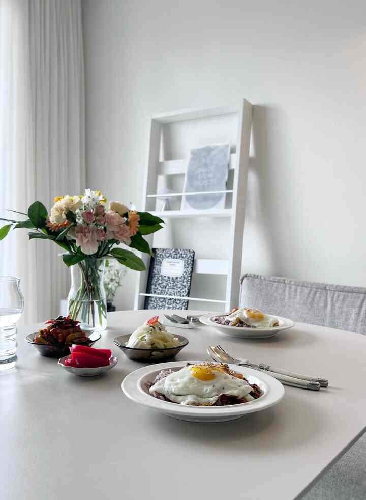 明るいホワイトトーンのダイニングルーム、白いダイニングテーブルに皿とカトラリー、花瓶が配置されたナチュラルで清潔感のあるインテリア