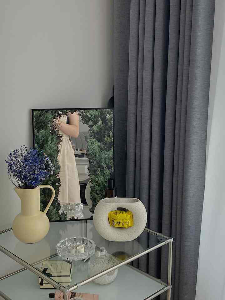 Modern objet space featuring gray curtains, an ivory vase, and a poster mirror with forest imagery