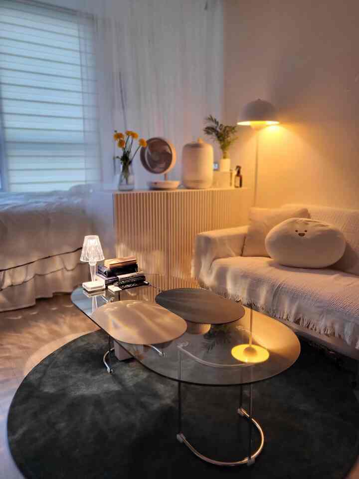 A cozy studio living room with warm lighting featuring a white sofa and dark gray round rug creating a harmonious atmosphere