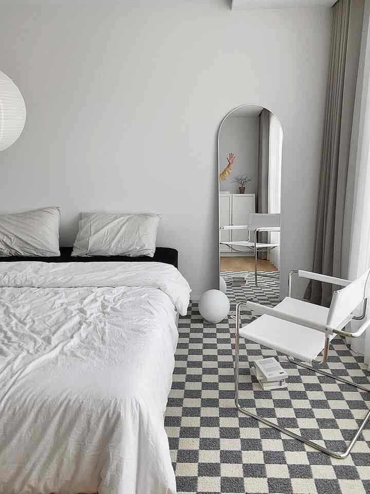 White and gray toned bedroom featuring a checkerboard rug, full-length mirror, and armchair with a modern, simple atmosphere