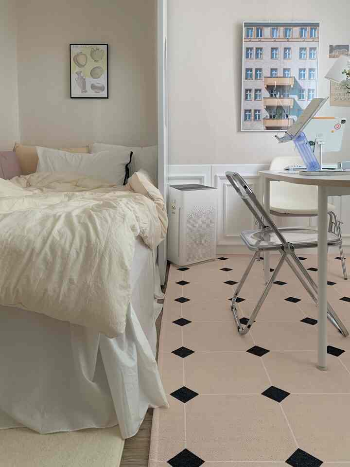 White and beige toned studio bedroom featuring a folding transparent chair and desk, creating a cozy and neat atmosphere